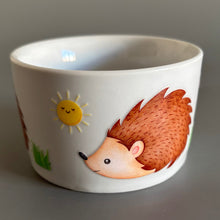 Load image into Gallery viewer, White ceramic bowl with hedgehog and sun design on a gray background