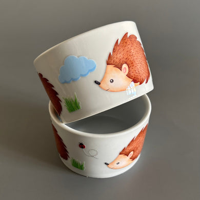 Two ceramic bowls with hedgehog illustrations on a gray background